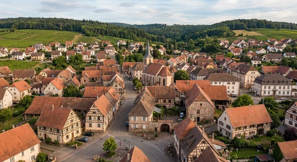 Photographie a&eacute;rienne ou vue panoramique de la commune de Mutzig en Alsace (Bas-Rhin), montrant un environnement r&eacute;sidentiel typique avec habitations, toitures, rues et espaces p&eacute;riurbains. L'image doit transmettre un sentiment de proximit&eacute; locale et repr&eacute;senter une petite commune alsacienne o&ugrave; intervient l'entreprise de r&eacute;novation, visuellement distincte d'une vue similaire de Fegersheim.