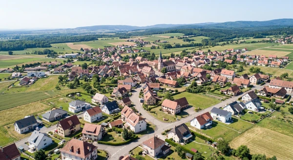 Photographie a&eacute;rienne ou vue panoramique de la commune d'Innenheim en Alsace (Bas-Rhin), montrant un environnement r&eacute;sidentiel typique avec habitations, toitures, rues et espaces p&eacute;riurbains. L'image doit transmettre un sentiment de proximit&eacute; locale et repr&eacute;senter une petite commune alsacienne o&ugrave; intervient l'entreprise de r&eacute;novation, visuellement distincte des vues panoramiques de Fegersheim et Mutzig d&eacute;j&agrave; utilis&eacute;es. La perspective a&eacute;rienne doit clairement identifier Innenheim comme une commune alsacienne avec ses caract&eacute;ristiques architecturales propres.