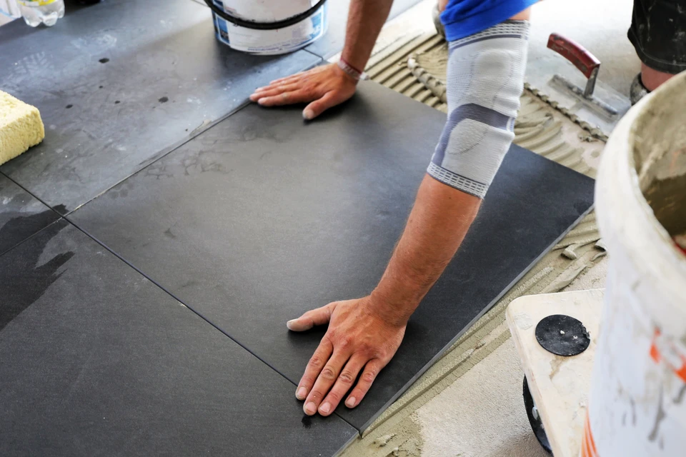 Artisan posant du carrelage gris anthracite sur chape ciment avec adh&eacute;sif