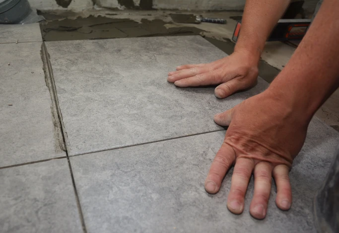 Artisan carreleur installant du carrelage gris sur chantier intérieur