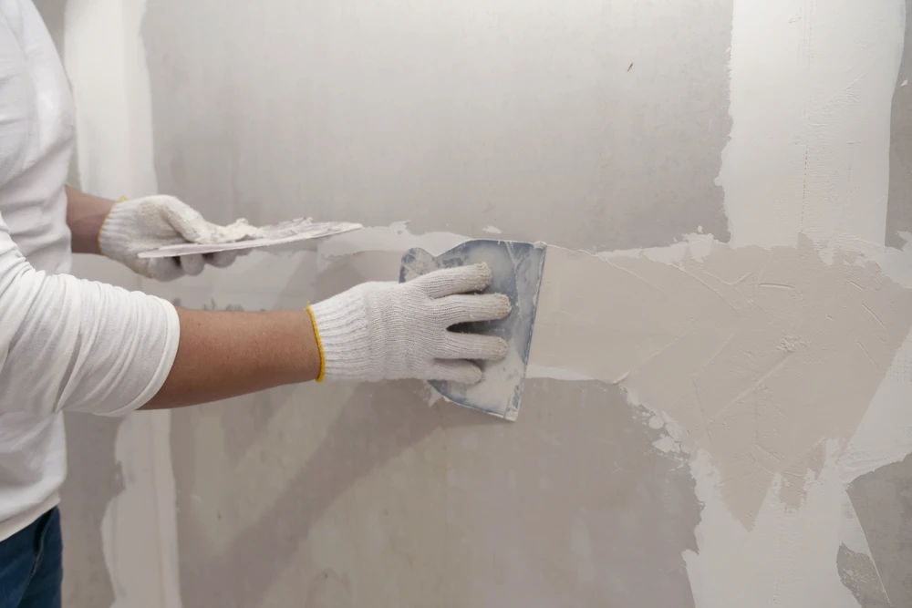Ouvrier en bâtiment travaillant sur une cloison intérieure, portant casque de sécurité blanc et lunettes de protection