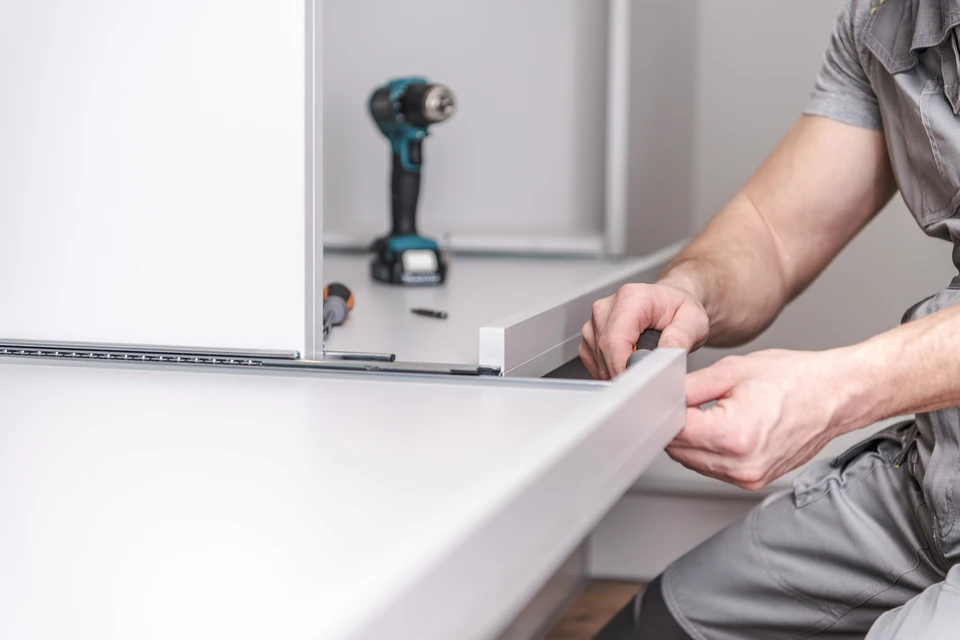 Ouvrier en uniforme gris installant des éléments de cuisine blanche dans un intérieur résidentiel moderne